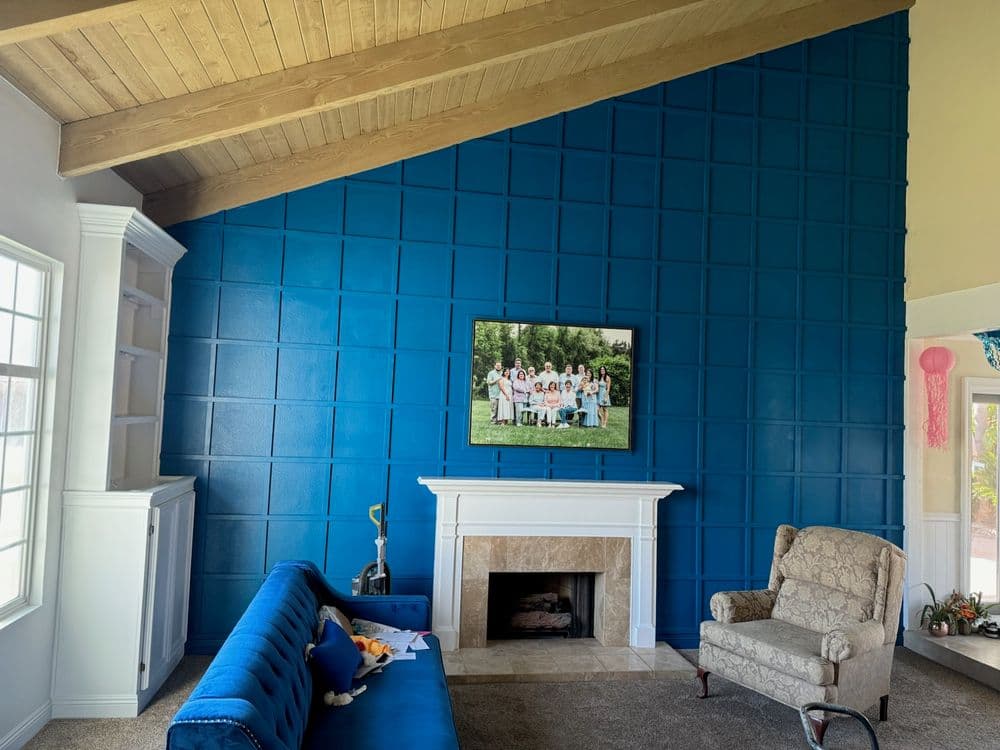 Blue accent wall in a living room with a fireplace and a vintage armchair, featuring a family portrait.