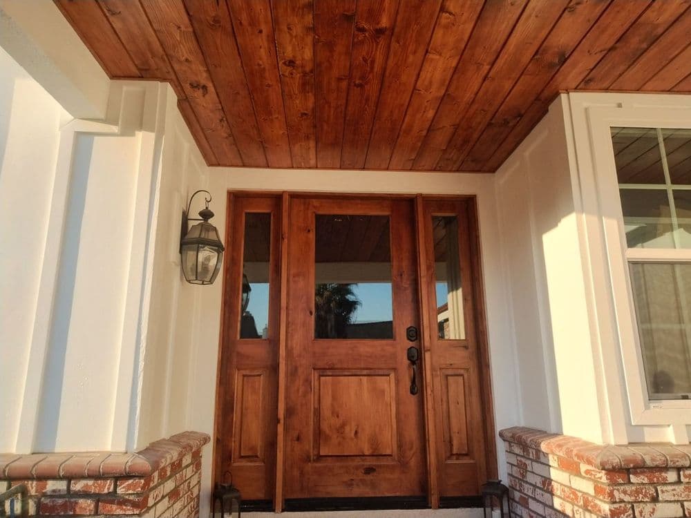Wooden double front doors under a rustic ceiling, framed by white walls and brick steps.
