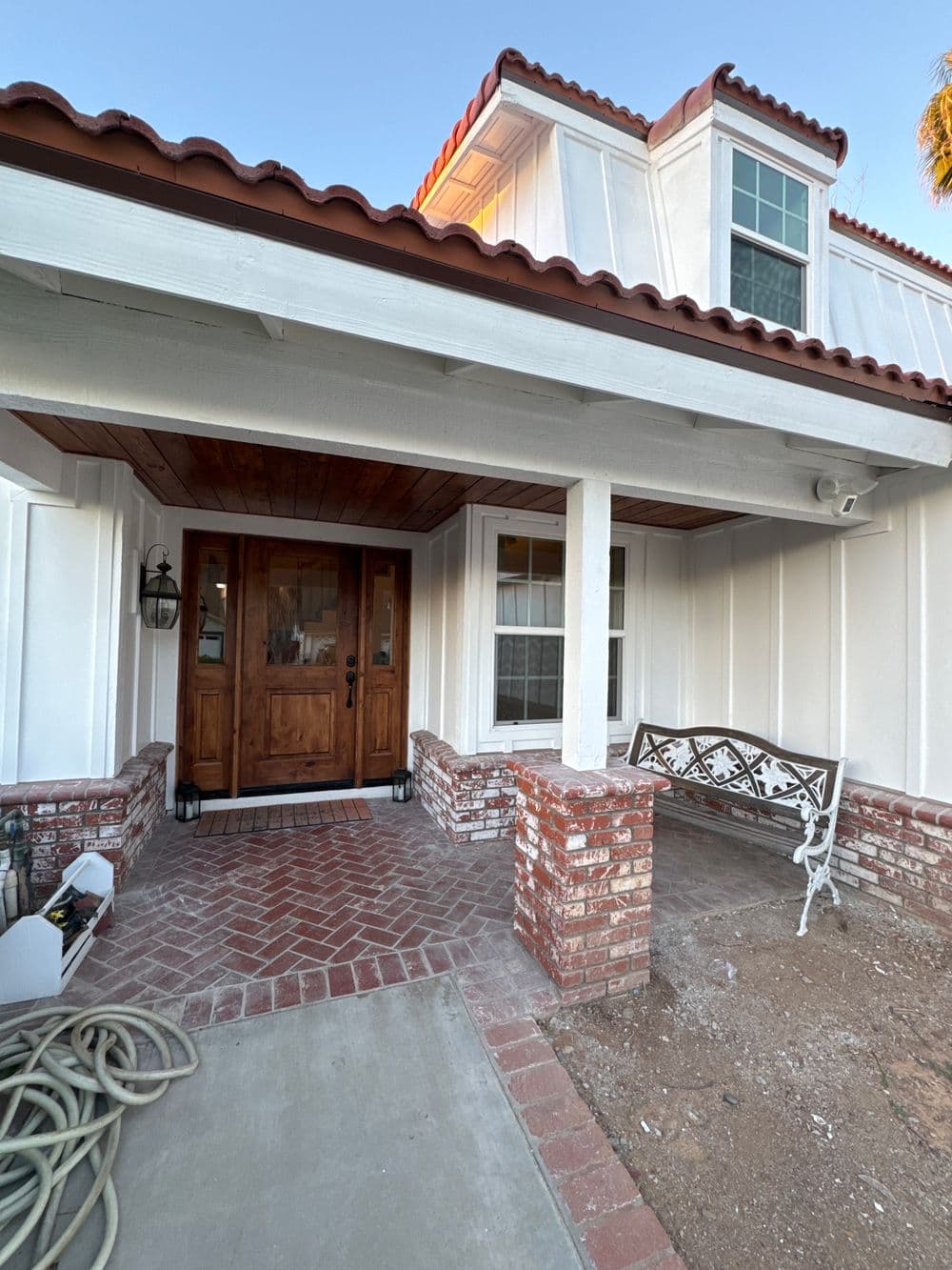 Front porch of a home with a wooden door, white walls, and a brick pathway.